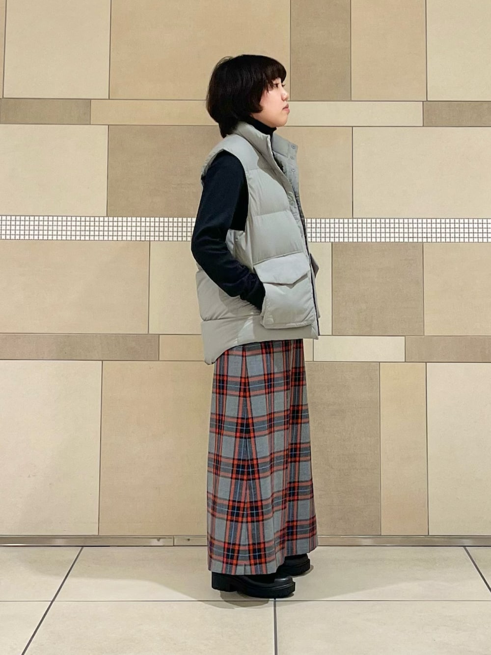 グレー系のダウンベスト、ブラック系のTシャツ/カットソー、グレー系のスカートを着用したレディースの秋コーディネートの3枚目の写真