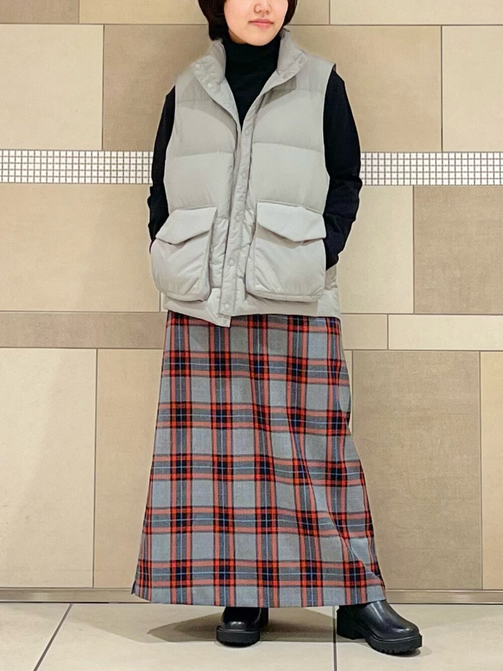 グレー系のダウンベスト、ブラック系のTシャツ/カットソー、グレー系のスカートを着用したレディースの秋コーディネートの2枚目の写真