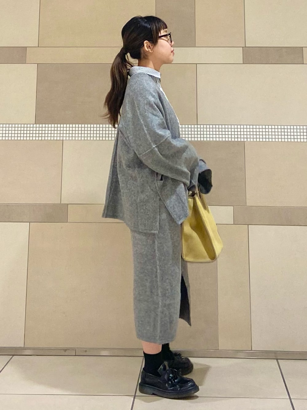 イエロー系のショルダーバッグ、グレー系のカーディガン/ボレロ、グレー系のスカートを着用したレディースの秋コーディネートの2枚目の写真