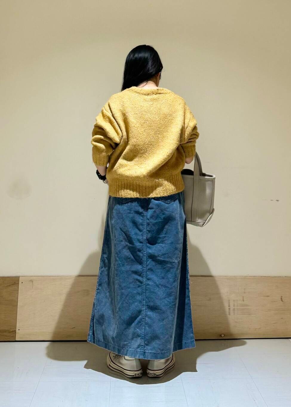 ベージュ系のトートバッグ、イエロー系のニット/セーター、ブルー系のスカートを着用したレディースの冬コーディネートの3枚目の写真