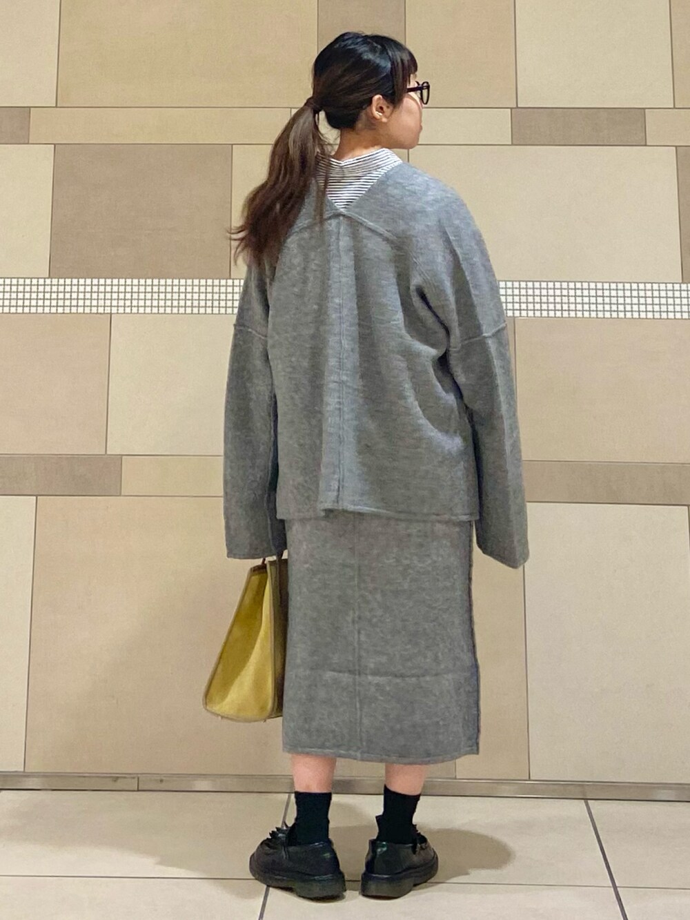 イエロー系のショルダーバッグ、グレー系のカーディガン/ボレロ、グレー系のスカートを着用したレディースの秋コーディネートの3枚目の写真