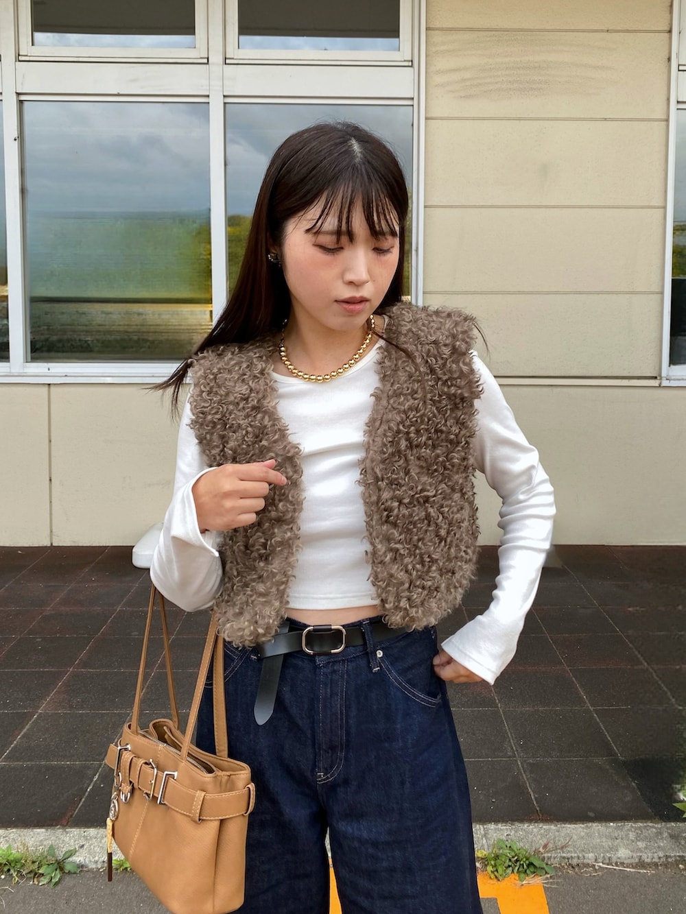 ブラウン系のベスト、ブラウン系のハンドバッグ、ベージュ系のスニーカーを着用したレディースの秋コーディネートの3枚目の写真