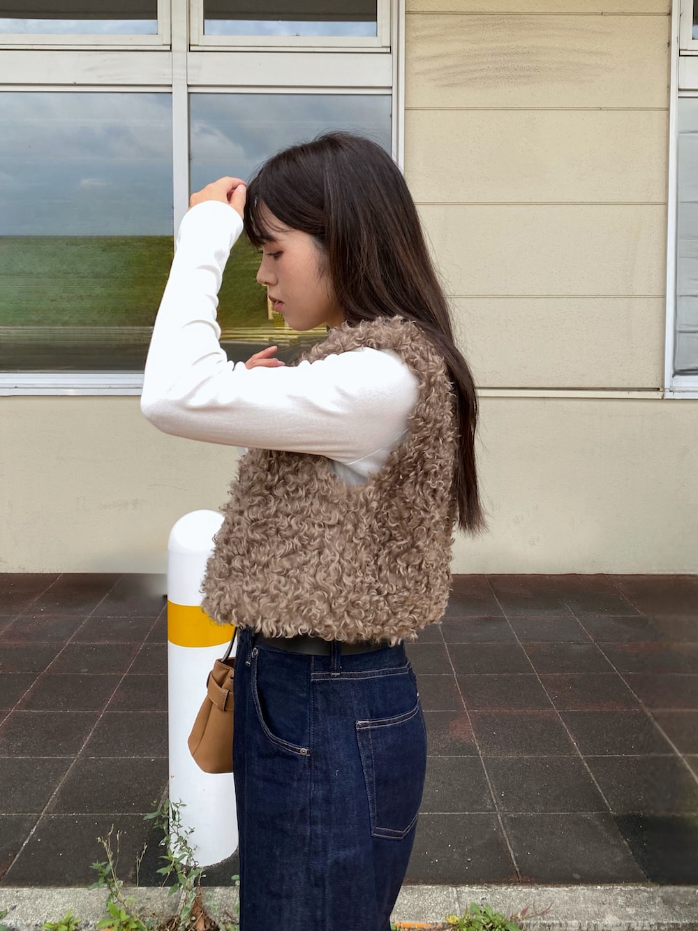 ブラウン系のベスト、ブラウン系のハンドバッグ、ベージュ系のスニーカーを着用したレディースの秋コーディネートの2枚目の写真