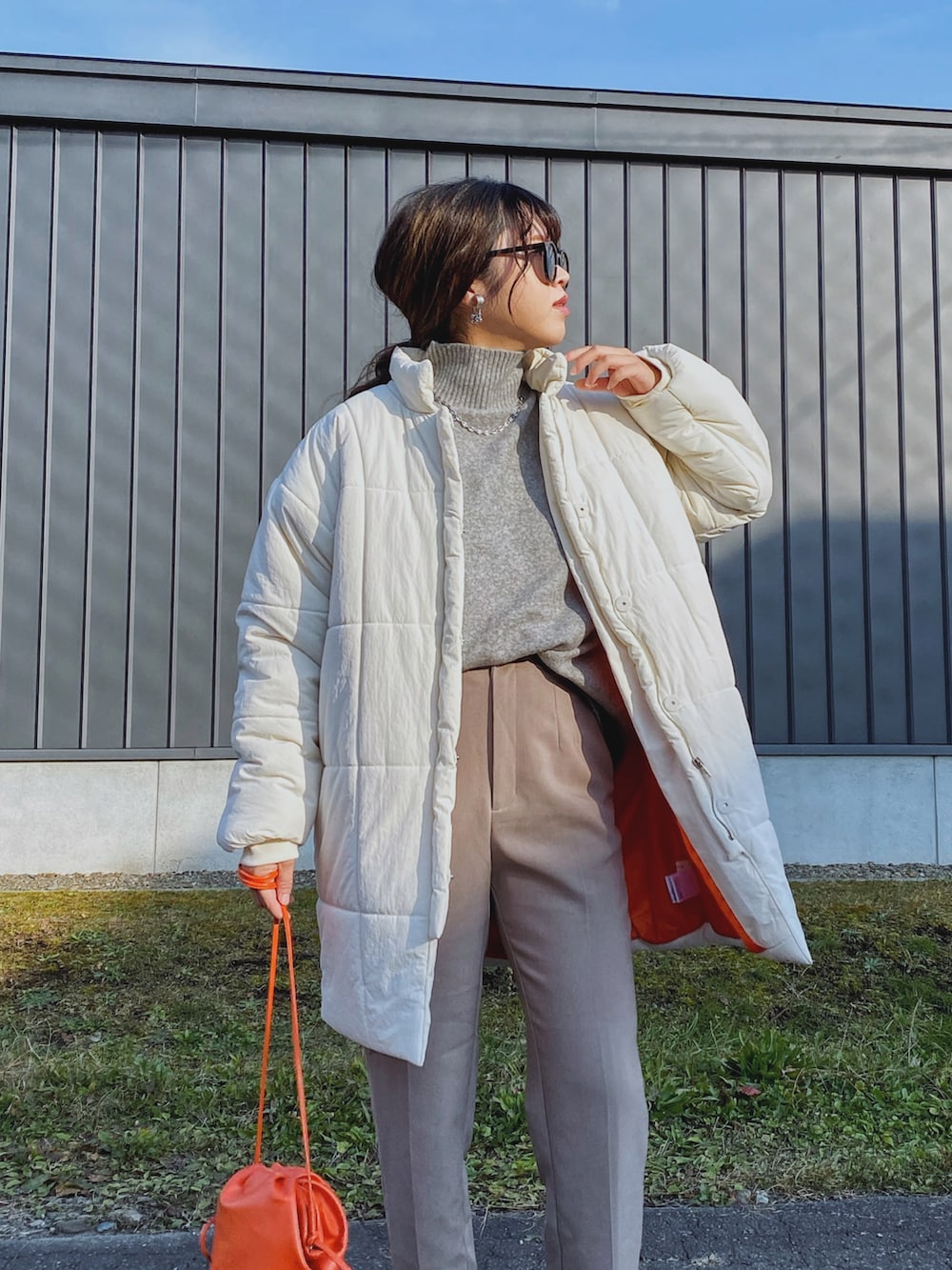 ホワイト系のダウンジャケット/コート、オレンジ系のショルダーバッグ、グレー系のニット/セーターを着用したレディースの秋コーディネートの4枚目の写真