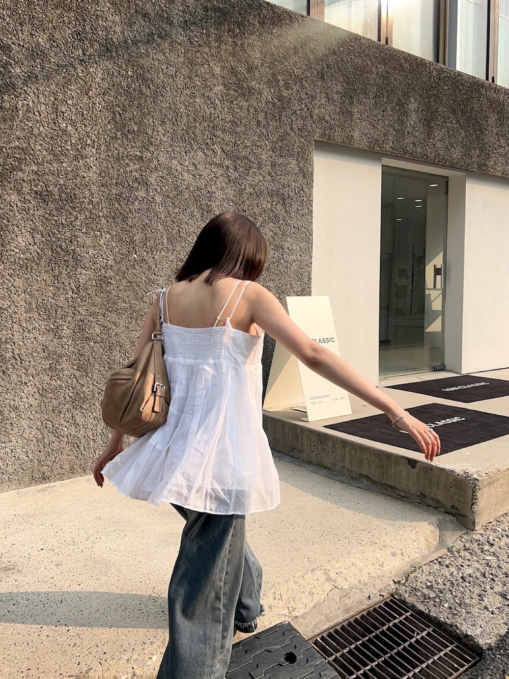 ブルー系のデニムパンツ、ブラック系のスニーカー、ベージュ系のバッグを着用したレディースの夏コーディネートの2枚目の写真