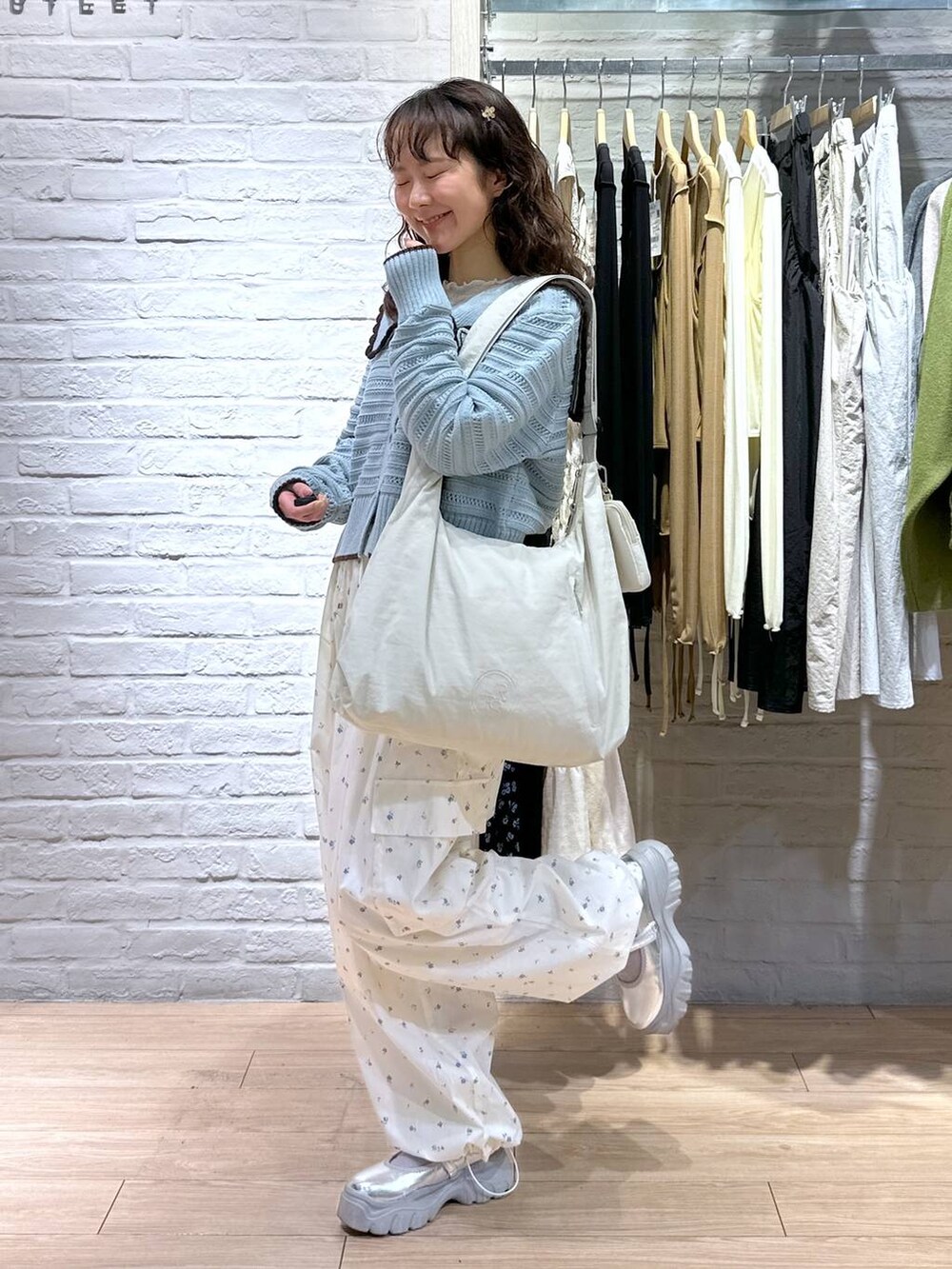 ベージュ系のショルダーバッグ、ホワイト系のTシャツ/カットソー、ブルー系のニット/セーターを着用したレディースの春コーディネートの2枚目の写真