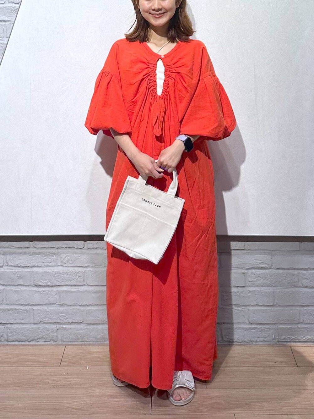 オレンジ系のワンピース、ホワイト系のトートバッグ、ホワイト系のサンダルを着用したレディースの夏コーディネートの2枚目の写真