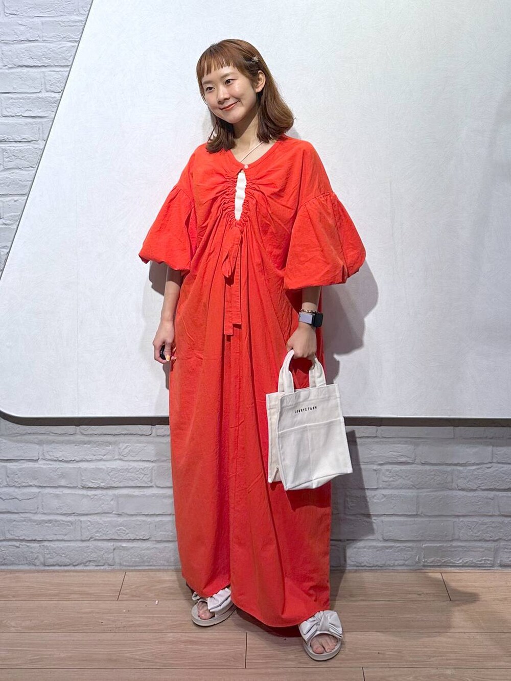 オレンジ系のワンピース、ホワイト系のトートバッグ、ホワイト系のサンダルを着用したレディースの夏コーディネートの5枚目の写真