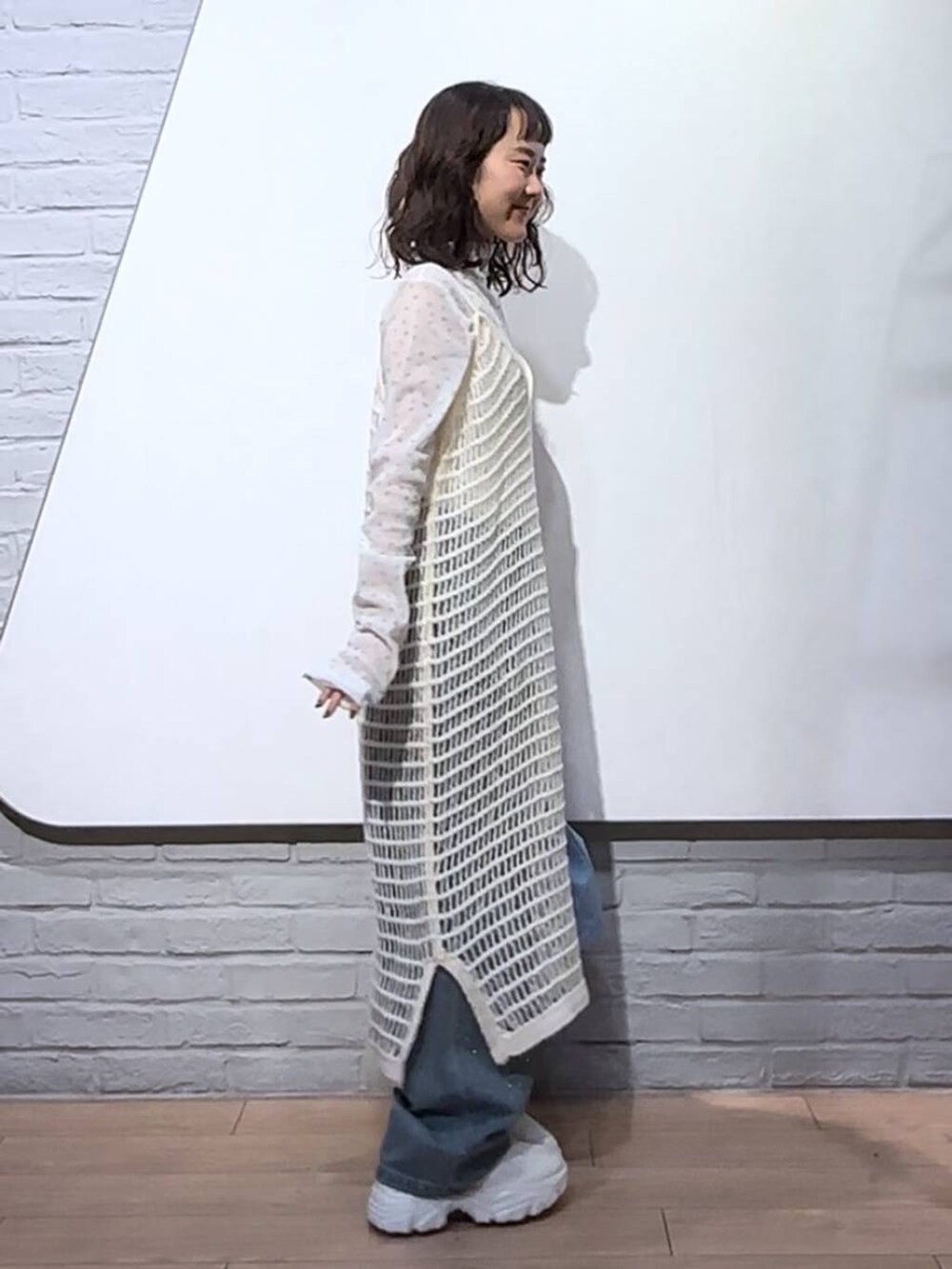 ブルー系のデニムパンツ、ホワイト系のワンピース、ブルー系のハンドバッグを着用したレディースの秋コーディネートの3枚目の写真