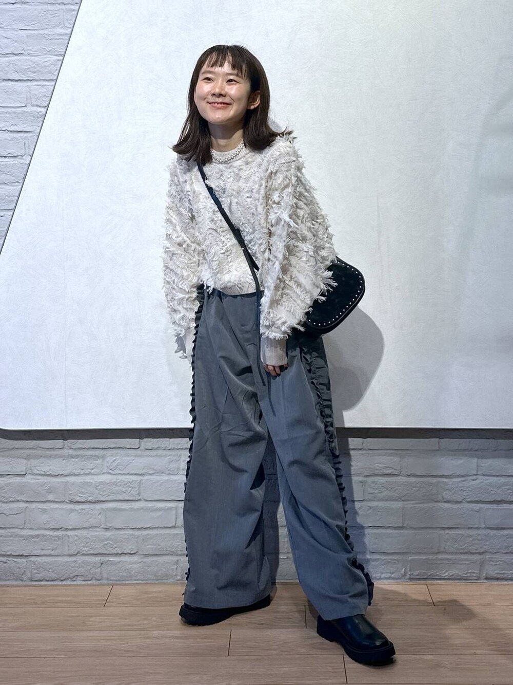 ブラック系のショルダーバッグ、ホワイト系のニット/セーター、ブラック系のブーツを着用したレディースの秋コーディネートの2枚目の写真