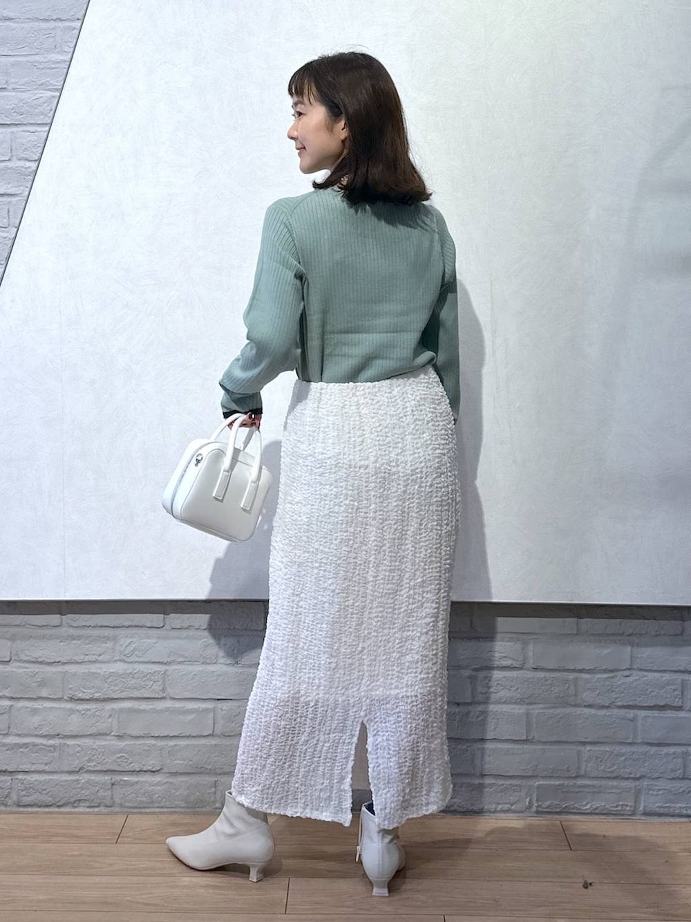 グリーン系のニット/セーター、ホワイト系のボストンバッグ、ホワイト系のブーツを着用したレディースの秋コーディネートの5枚目の写真