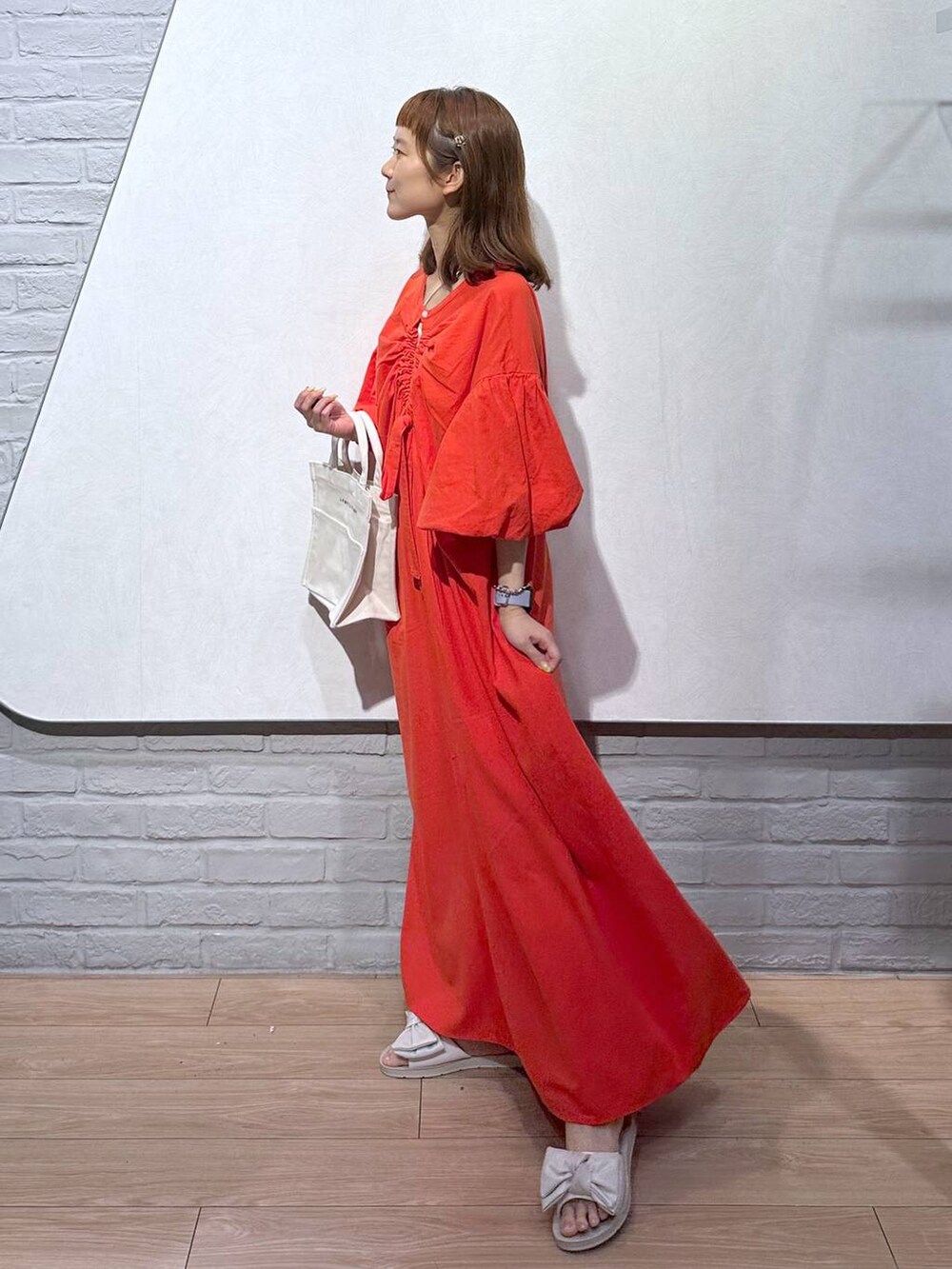 オレンジ系のワンピース、ホワイト系のトートバッグ、ホワイト系のサンダルを着用したレディースの夏コーディネートの3枚目の写真