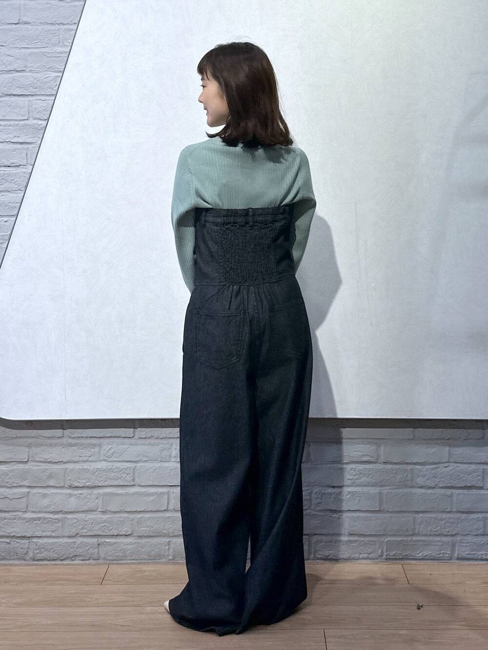 グリーン系のニット/セーター、ブラック系のサロペット/オーバーオール、グリーン系のボストンバッグを着用したレディースの秋コーディネートの4枚目の写真