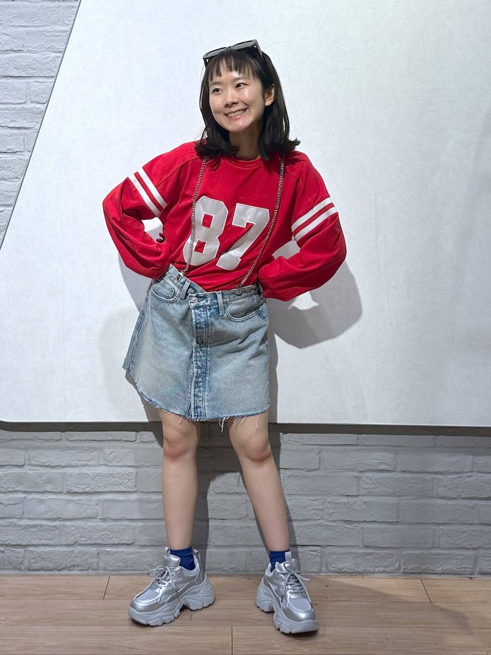 ブルー系のデニムスカート、シルバー系のスニーカー、レッド系のTシャツ/カットソーを着用したレディースの秋コーディネートの2枚目の写真