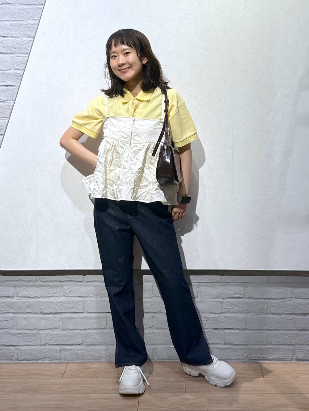 イエロー系のTシャツ/カットソー、ブラウン系のショルダーバッグ、ブルー系のデニムパンツを着用したレディースの秋コーディネートの2枚目の写真