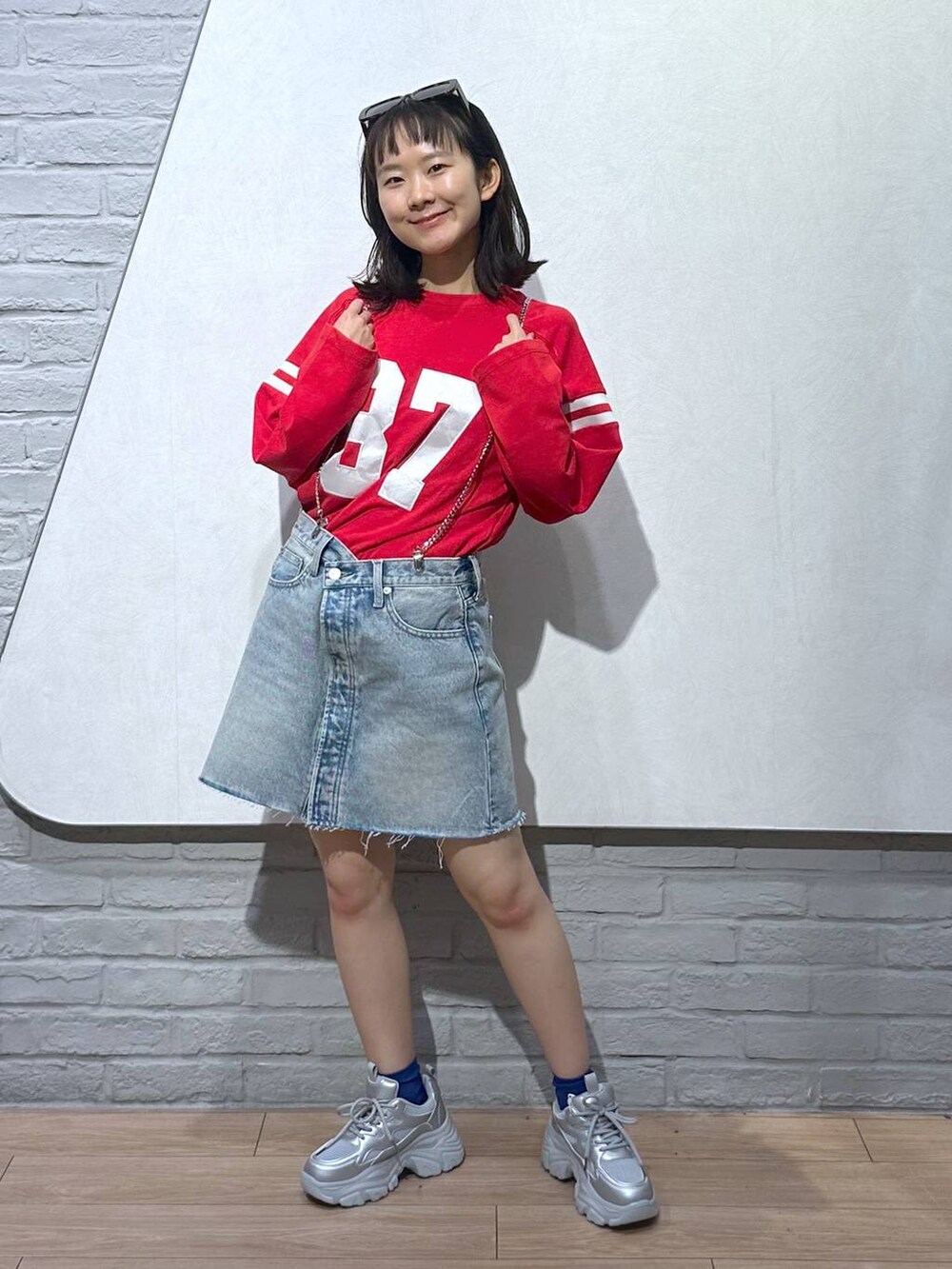 ブルー系のデニムスカート、シルバー系のスニーカー、レッド系のTシャツ/カットソーを着用したレディースの秋コーディネートの4枚目の写真