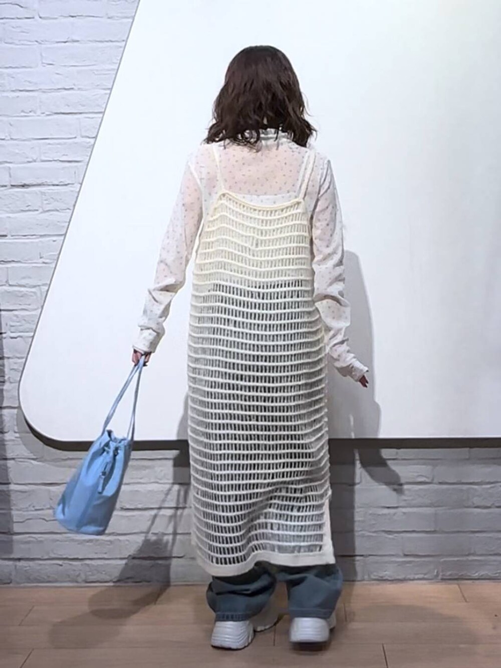 ブルー系のデニムパンツ、ホワイト系のワンピース、ブルー系のハンドバッグを着用したレディースの秋コーディネートの5枚目の写真