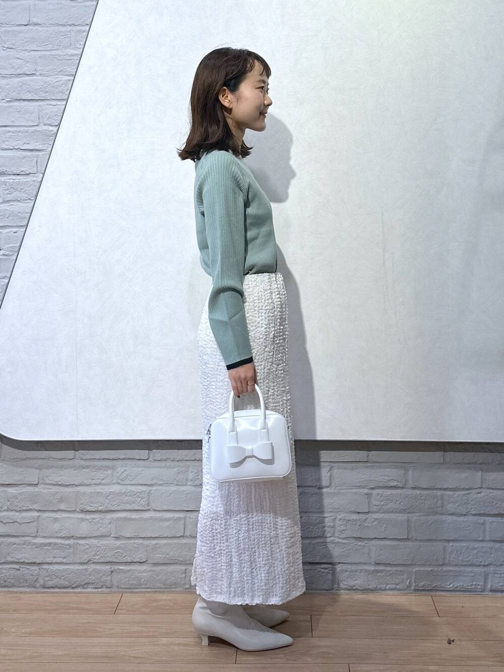 グリーン系のニット/セーター、ホワイト系のボストンバッグ、ホワイト系のブーツを着用したレディースの秋コーディネートの4枚目の写真
