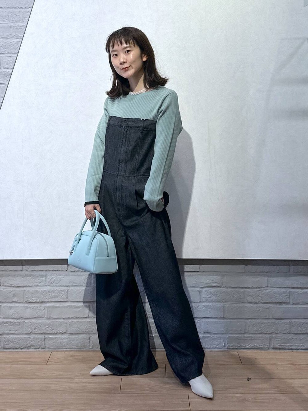 グリーン系のニット/セーター、ブラック系のサロペット/オーバーオール、グリーン系のボストンバッグを着用したレディースの秋コーディネートの2枚目の写真