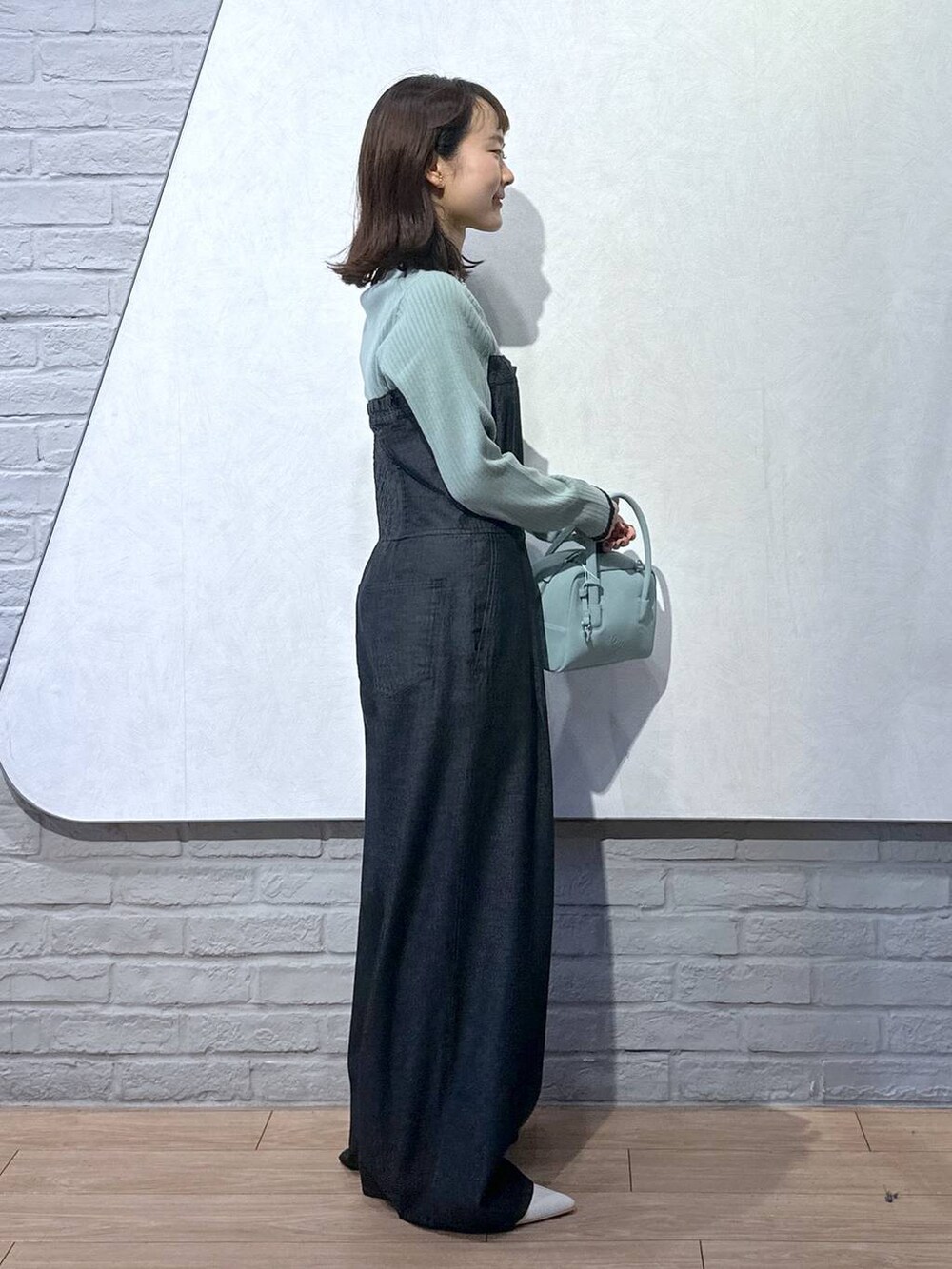 グリーン系のニット/セーター、ブラック系のサロペット/オーバーオール、グリーン系のボストンバッグを着用したレディースの秋コーディネートの3枚目の写真