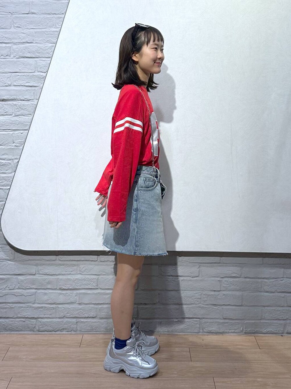 ブルー系のデニムスカート、シルバー系のスニーカー、レッド系のTシャツ/カットソーを着用したレディースの秋コーディネートの3枚目の写真