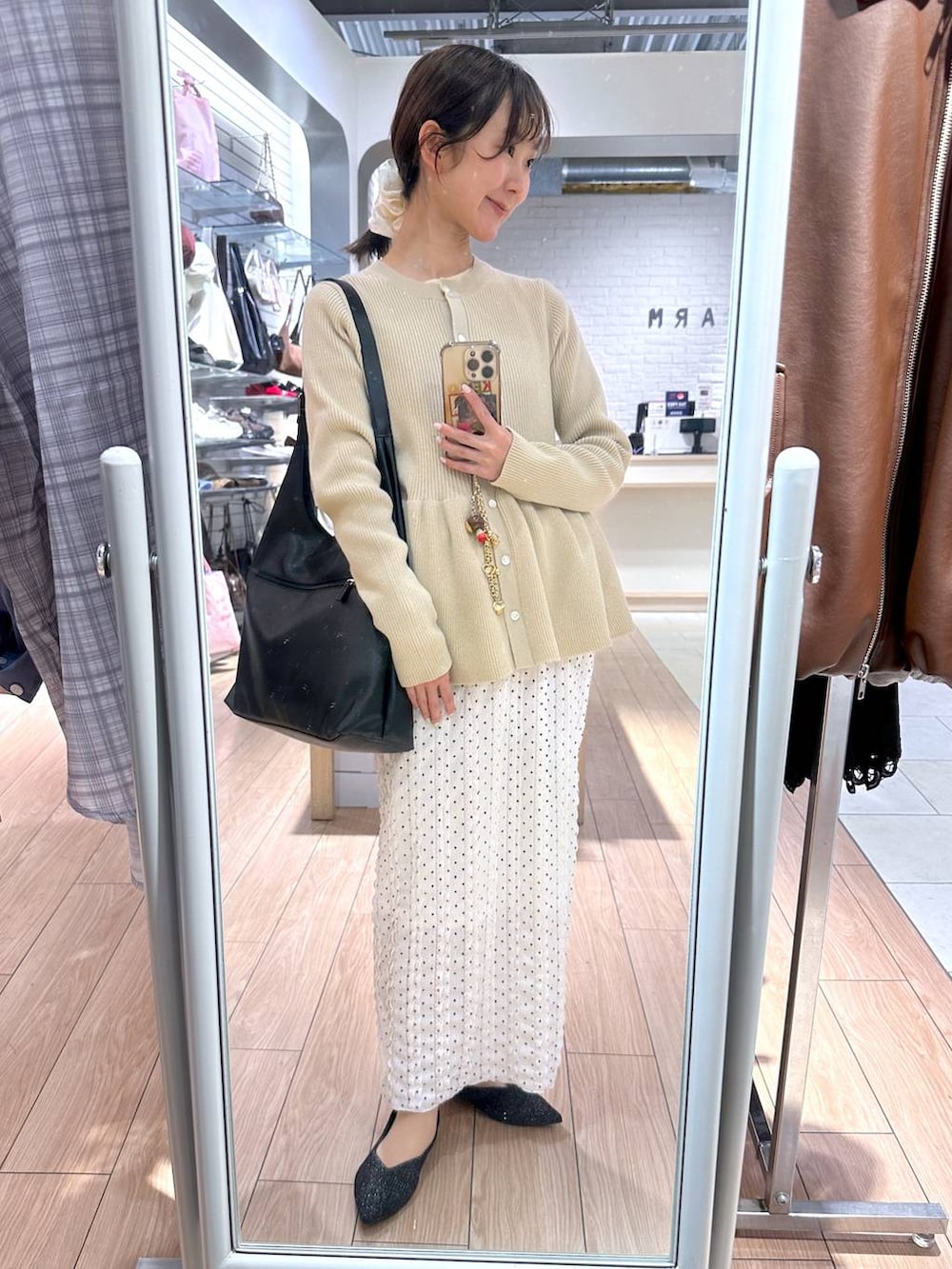 ブラック系のショルダーバッグ、ホワイト系のスカート、ホワイト系のカーディガン/ボレロを着用したレディースの春コーディネートの2枚目の写真