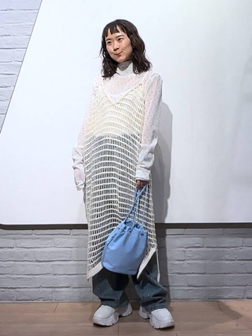 ブルー系のデニムパンツ、ホワイト系のワンピース、ブルー系のハンドバッグを着用したレディースの秋コーディネートの2枚目の写真