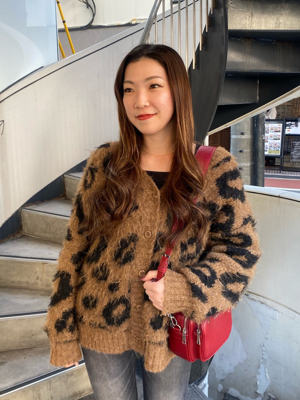 ブラック系のデニムパンツ、ブラウン系のニット/セーター、レッド系のショルダーバッグを着用したレディースの秋コーディネートの4枚目の写真