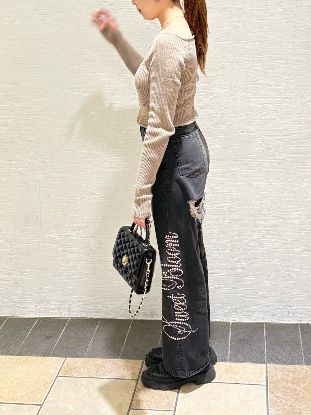 ブラック系のショルダーバッグ、ブラック系のデニムパンツ、ブラック系のブーツを着用したレディースの秋コーディネートの2枚目の写真