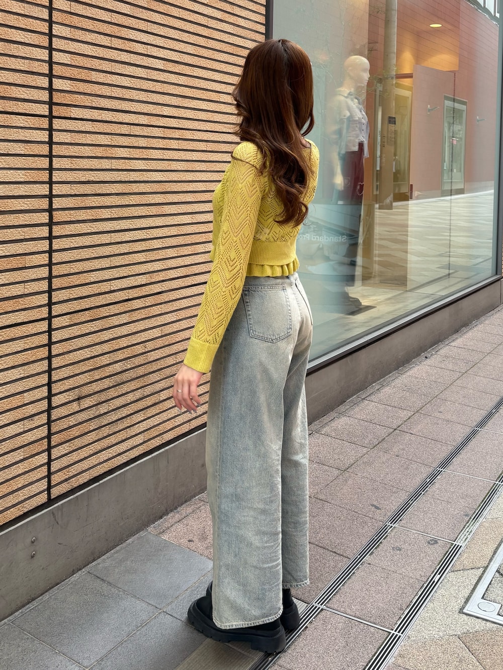イエロー系のカーディガン/ボレロ、ブラック系のブーツ、ブルー系のデニムパンツを着用したレディースの春コーディネートの2枚目の写真