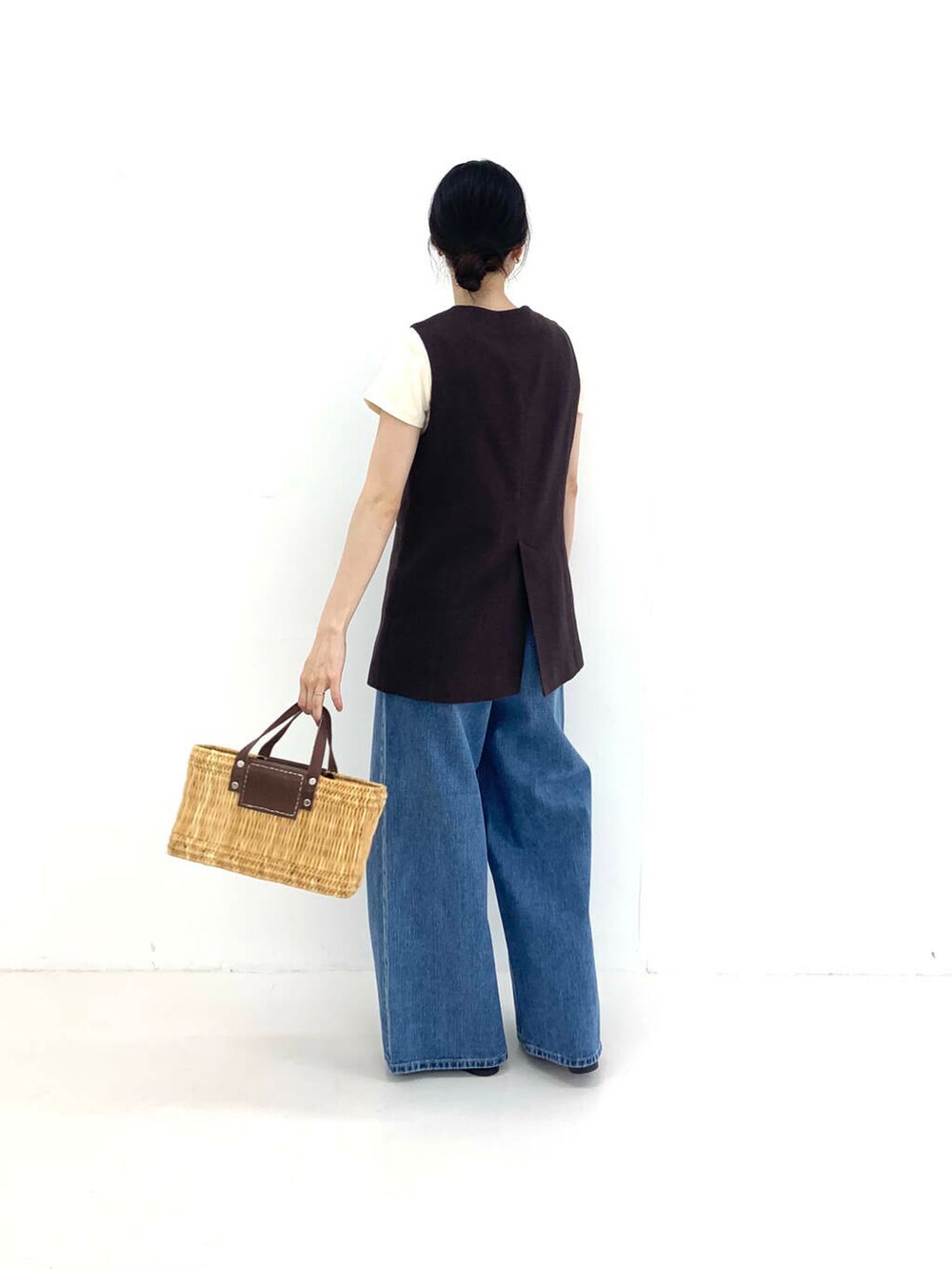 ブルー系のデニムパンツ、ブラウン系のかごバッグ、ブラウン系のベストを着用したレディースの夏コーディネートの2枚目の写真