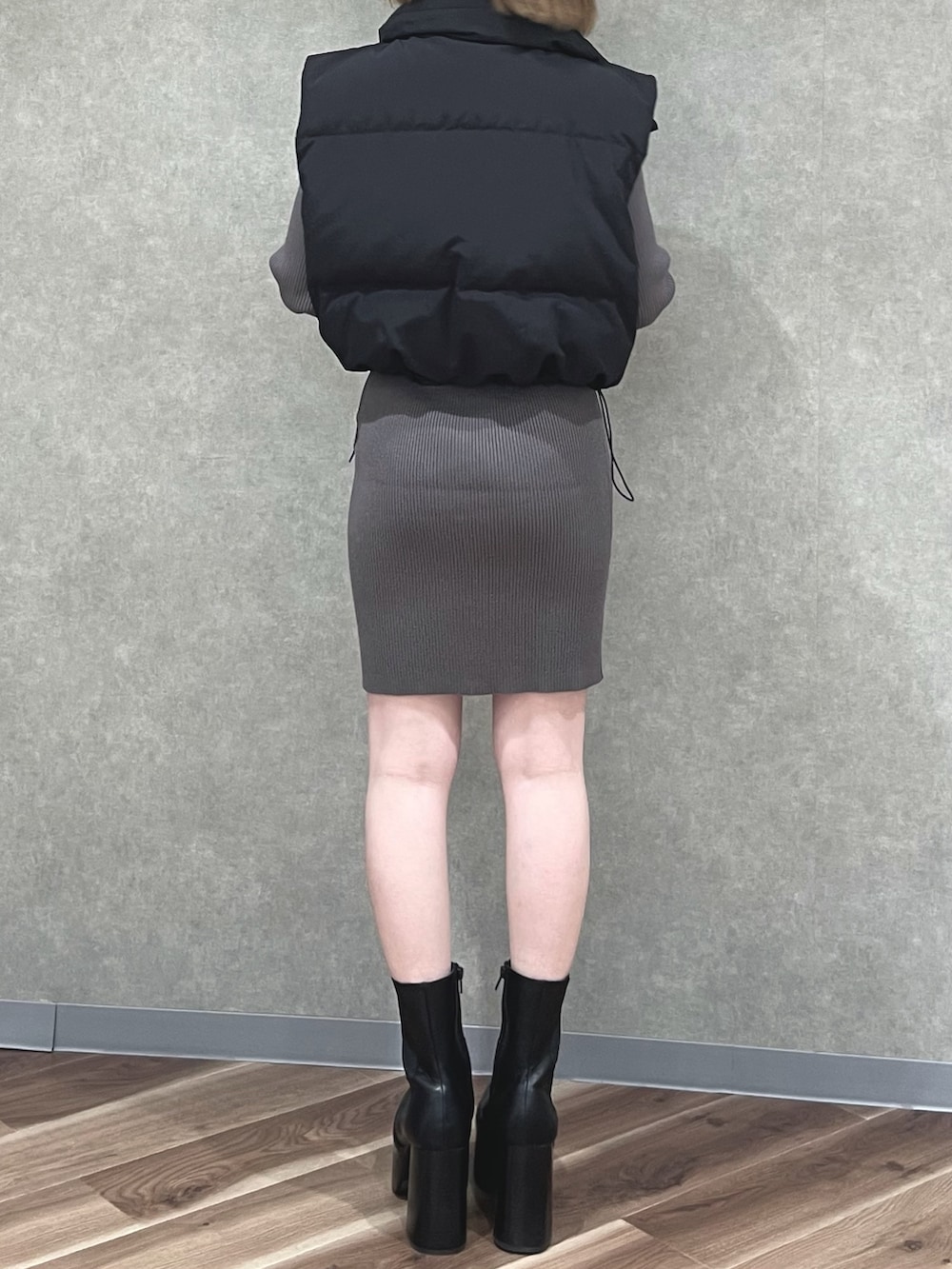 ブラック系のダウンベスト、グレー系のワンピース、ブラック系のブーツを着用したレディースの秋コーディネートの3枚目の写真