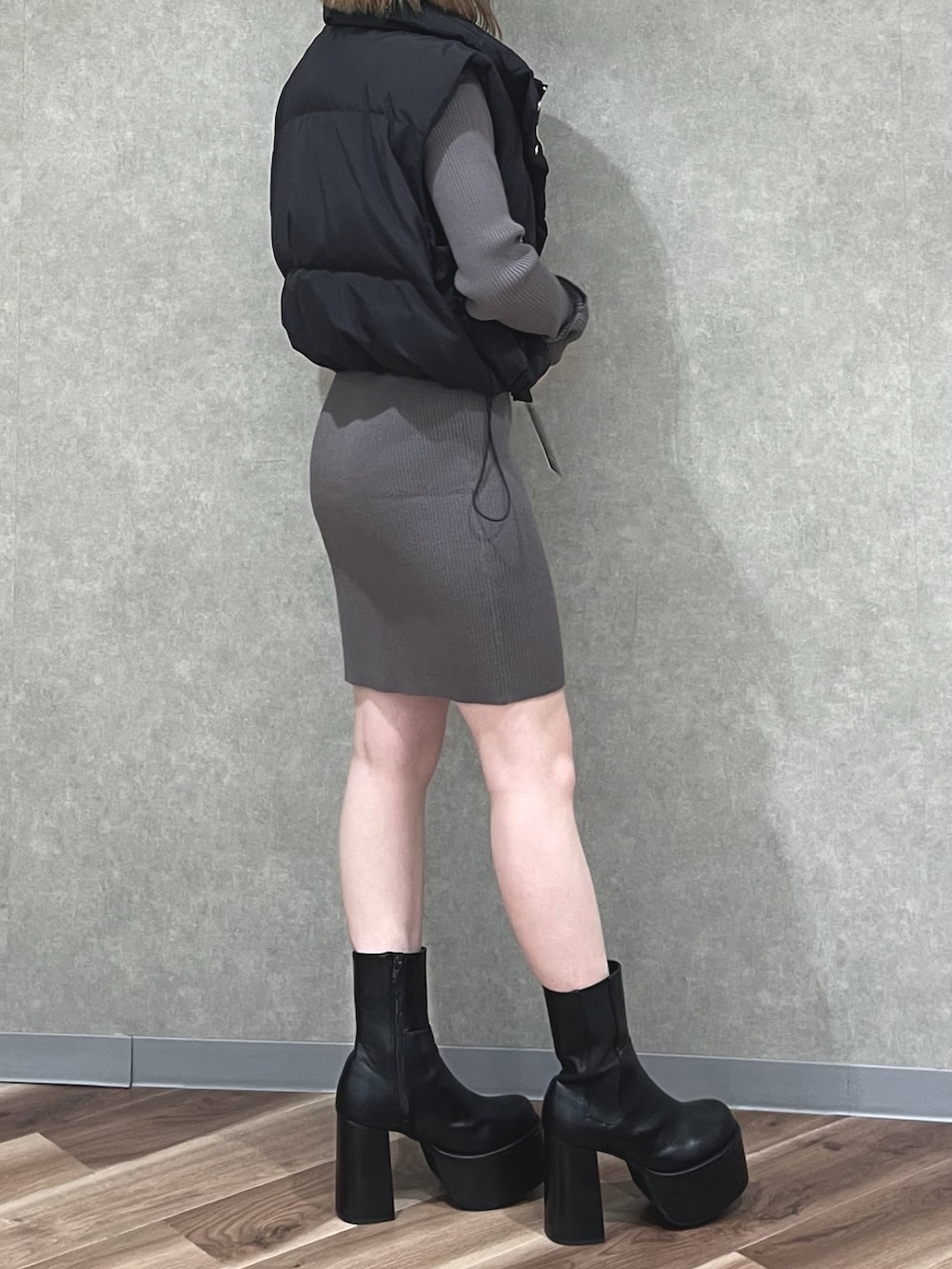 ブラック系のダウンベスト、グレー系のワンピース、ブラック系のブーツを着用したレディースの秋コーディネートの2枚目の写真