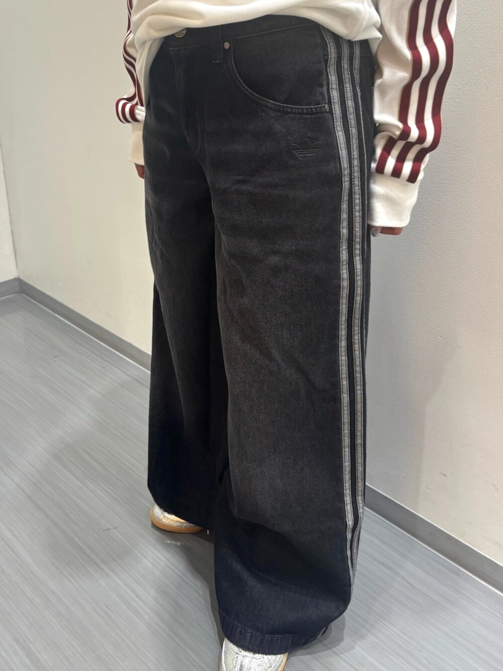 シルバー系のスニーカー、ブラック系のデニムパンツ、ホワイト系のポロシャツを着用したレディースの秋コーディネートの5枚目の写真