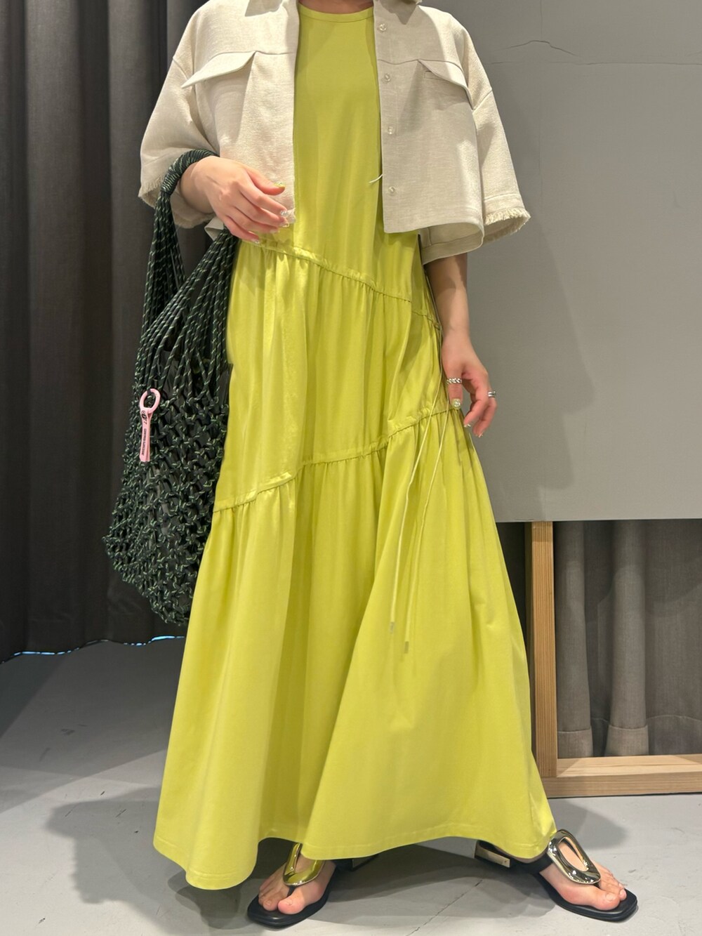 イエロー系のワンピース、ベージュ系のシャツ/ブラウス、ホワイト系のネックレスを着用したレディースの春コーディネートの3枚目の写真