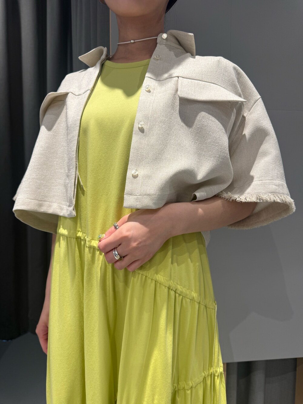 イエロー系のワンピース、ベージュ系のシャツ/ブラウス、ホワイト系のネックレスを着用したレディースの春コーディネートの2枚目の写真