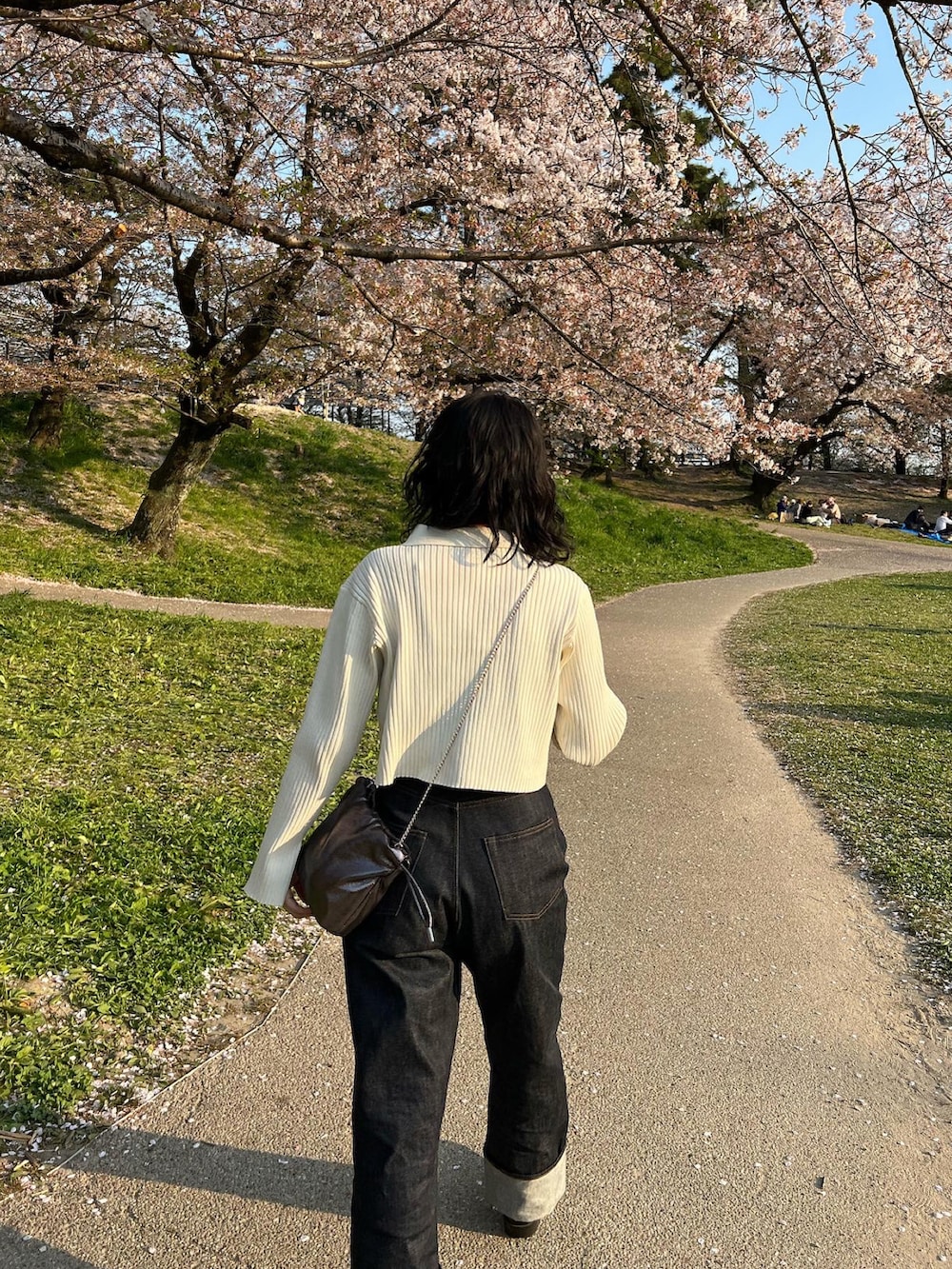 ホワイト系のニット/セーター、ブルー系のデニムパンツ、シルバー系のショルダーバッグを着用したレディースの春コーディネートの2枚目の写真