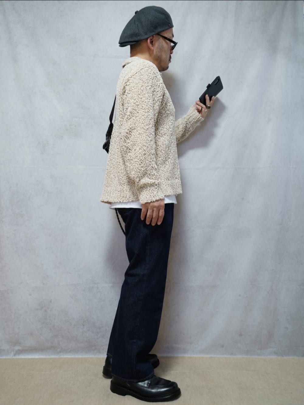 ブラック系のシューズ、ブルー系のデニムパンツ、ホワイト系のニット/セーターを着用したメンズの春コーディネートの4枚目の写真