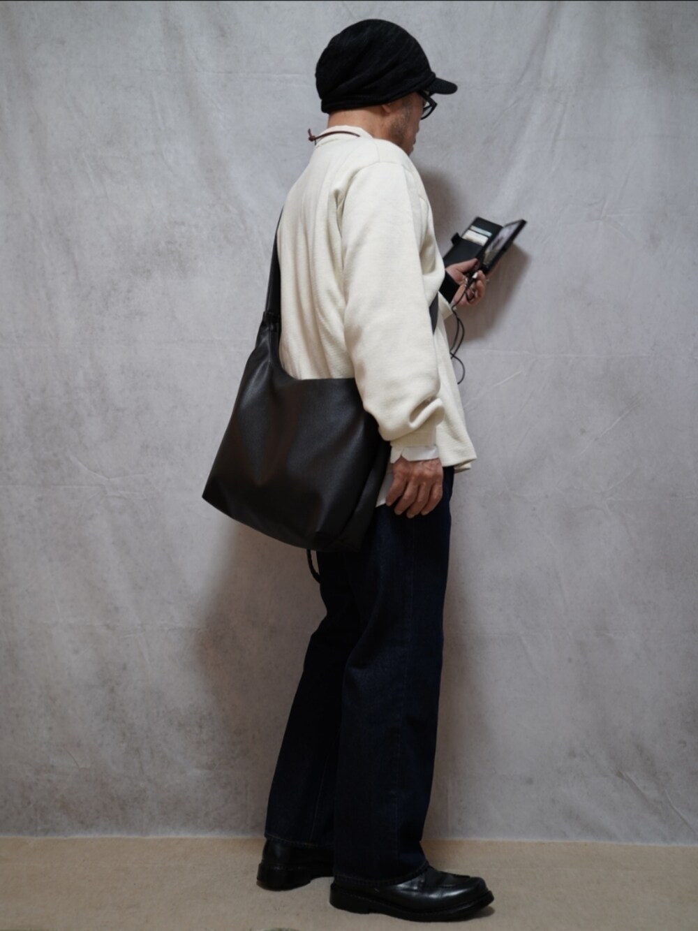 ブラック系のシューズ、ホワイト系のニット/セーター、ブルー系のデニムパンツを着用したメンズの春コーディネートの4枚目の写真