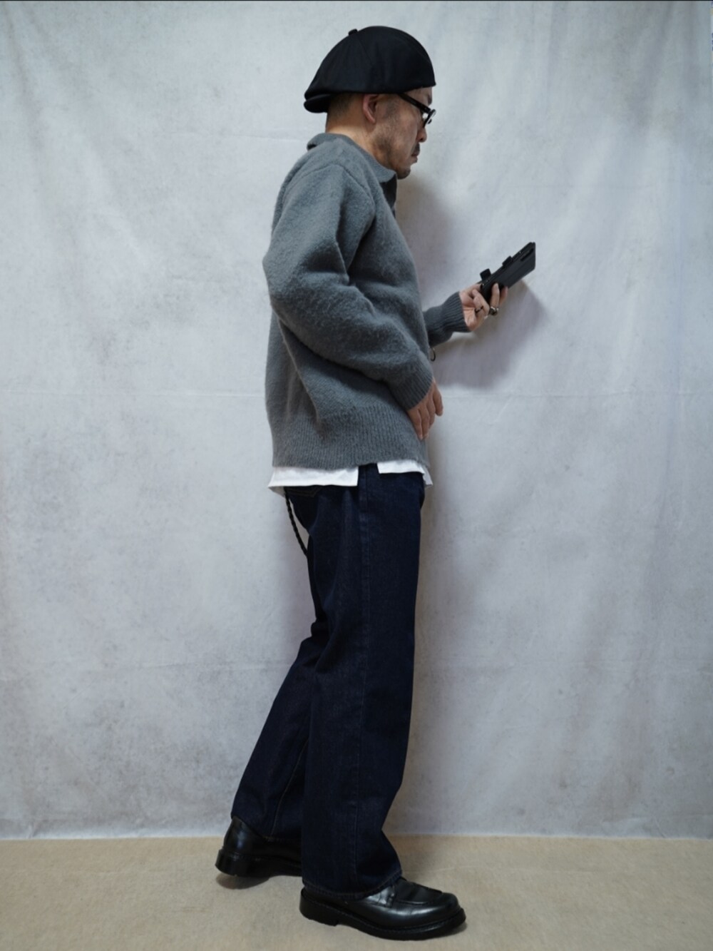 ブラック系のシューズ、ブルー系のデニムパンツ、グレー系のニット/セーターを着用したメンズの春コーディネートの4枚目の写真