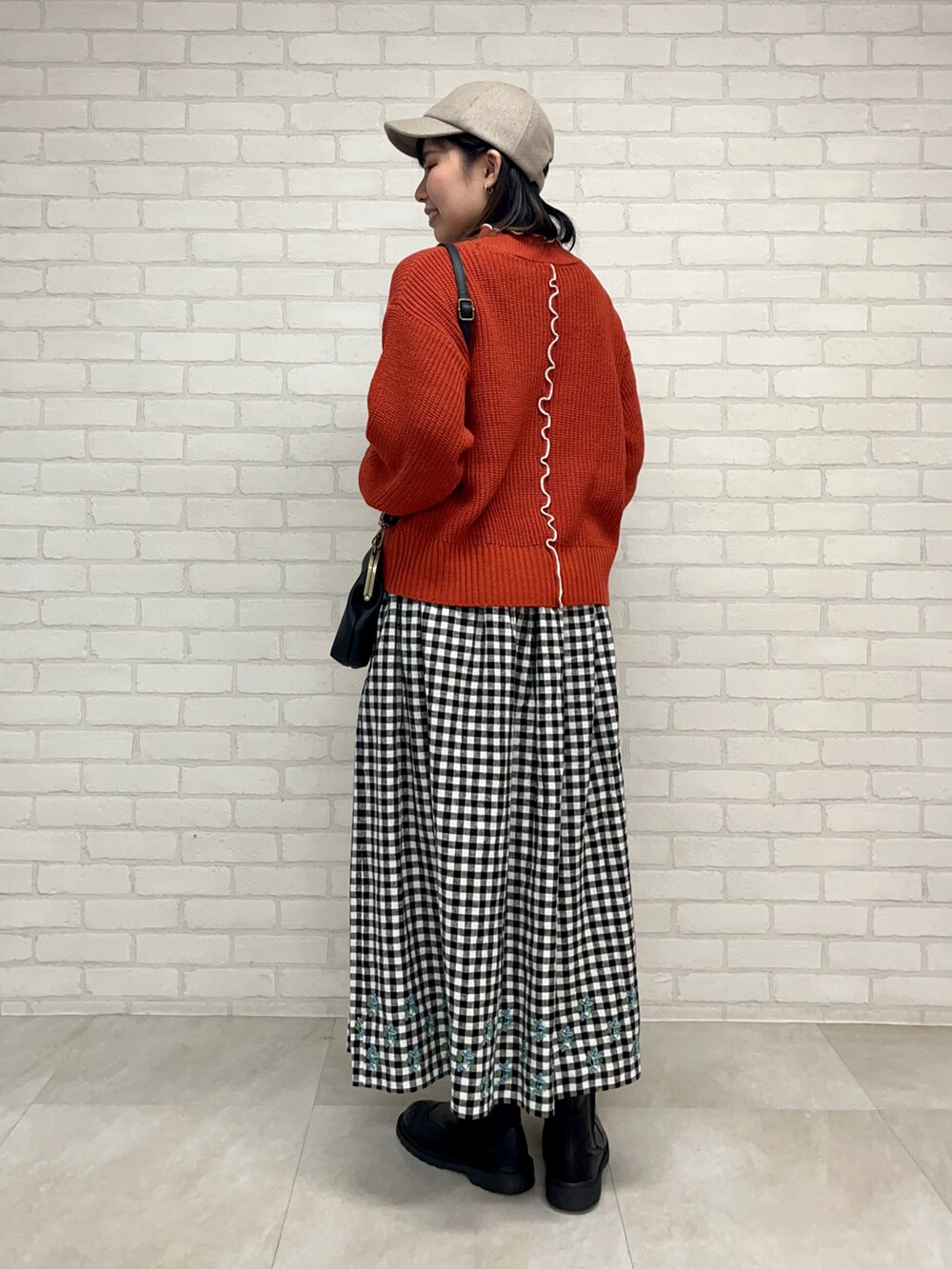 レッド系のニット/セーター、ブラック系のスカート、ブラック系のブーツを着用したレディースの秋コーディネートの3枚目の写真