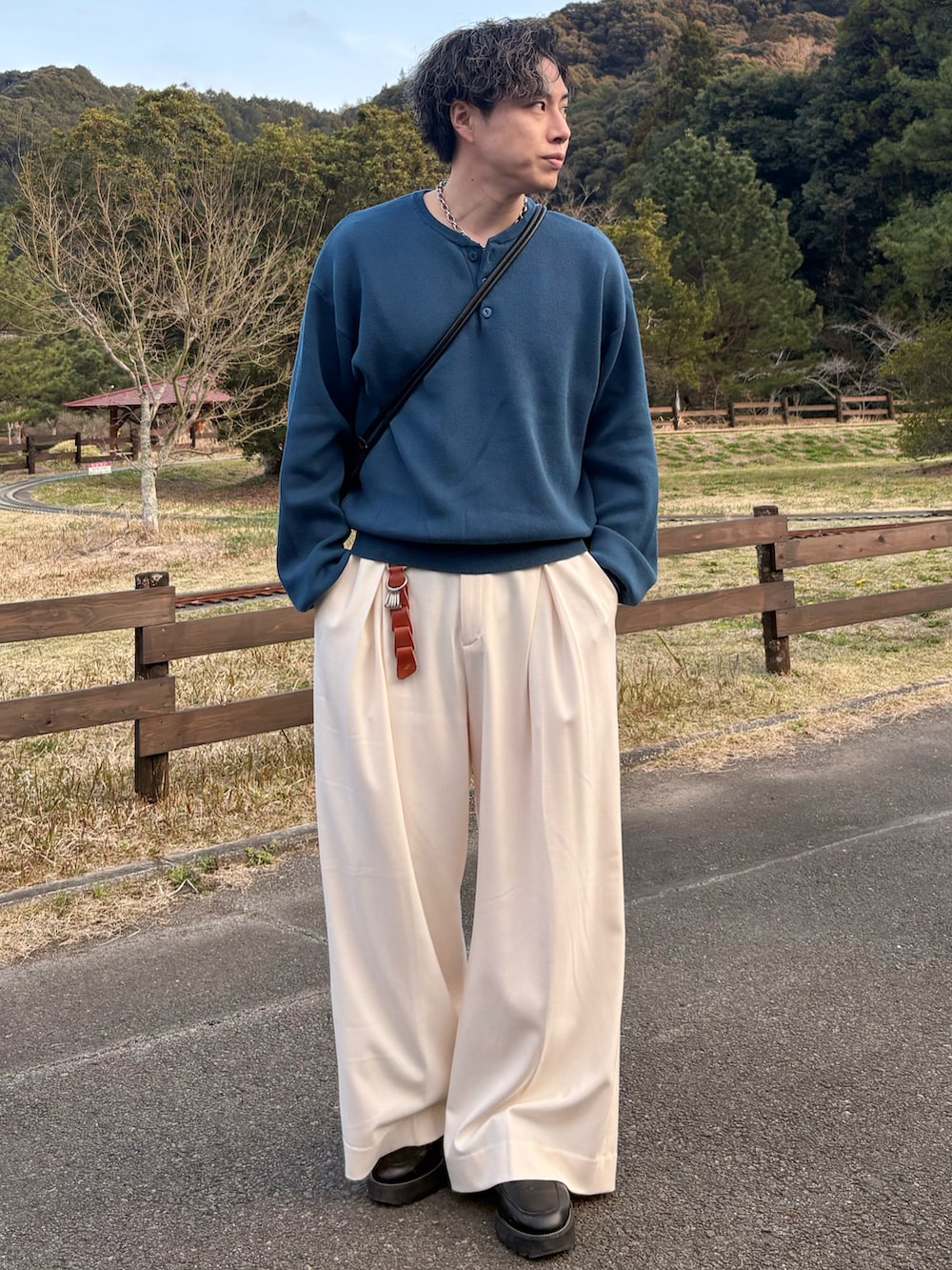 ブルー系のニット/セーター、ホワイト系のスラックス、ブラック系のショルダーバッグを着用したメンズの春コーディネートの2枚目の写真