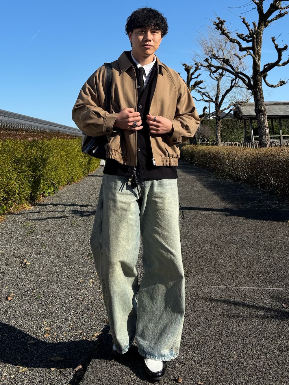 ブラック系のローファー、ブルー系のデニムパンツ、ブラック系のショルダーバッグを着用したメンズの春コーディネートの4枚目の写真