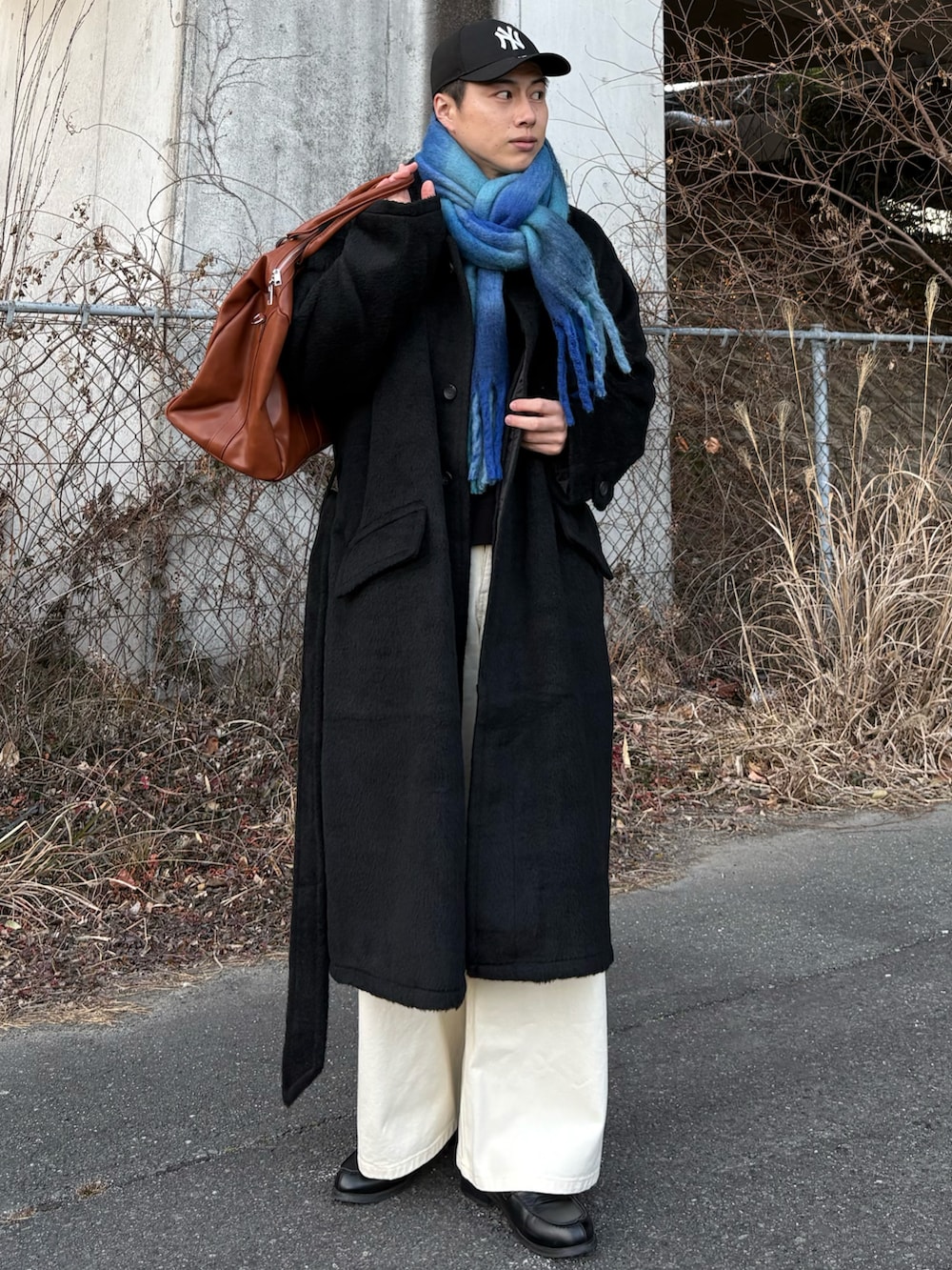 ブラック系のローファー、ブラック系のステンカラーコート、イエロー系のボストンバッグを着用したメンズの冬コーディネートの3枚目の写真