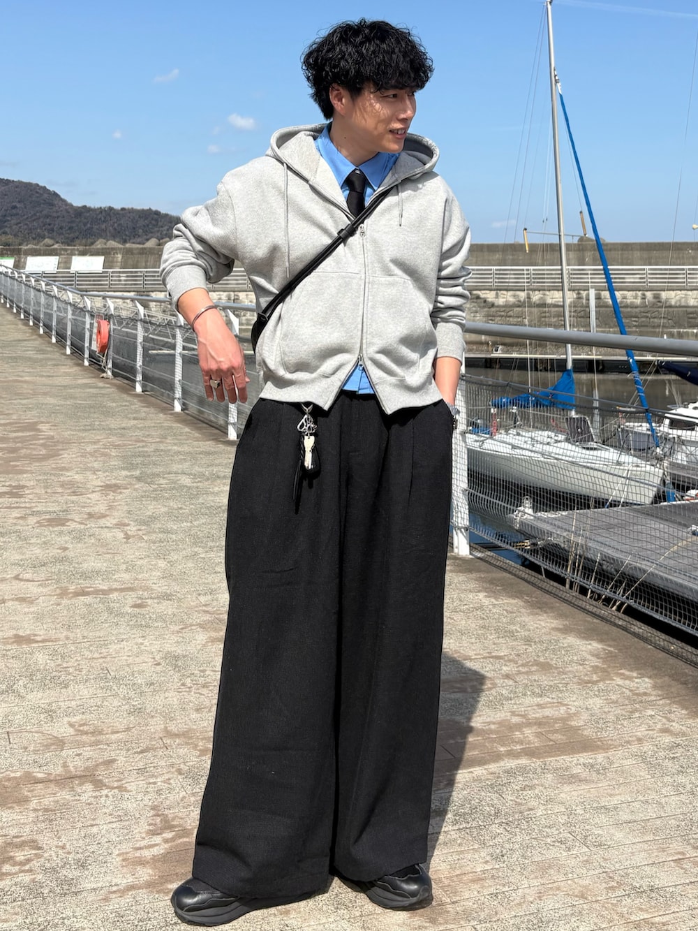 グレー系のスラックス、グレー系のパーカー、ブラック系のショルダーバッグを着用したメンズの春コーディネートの3枚目の写真