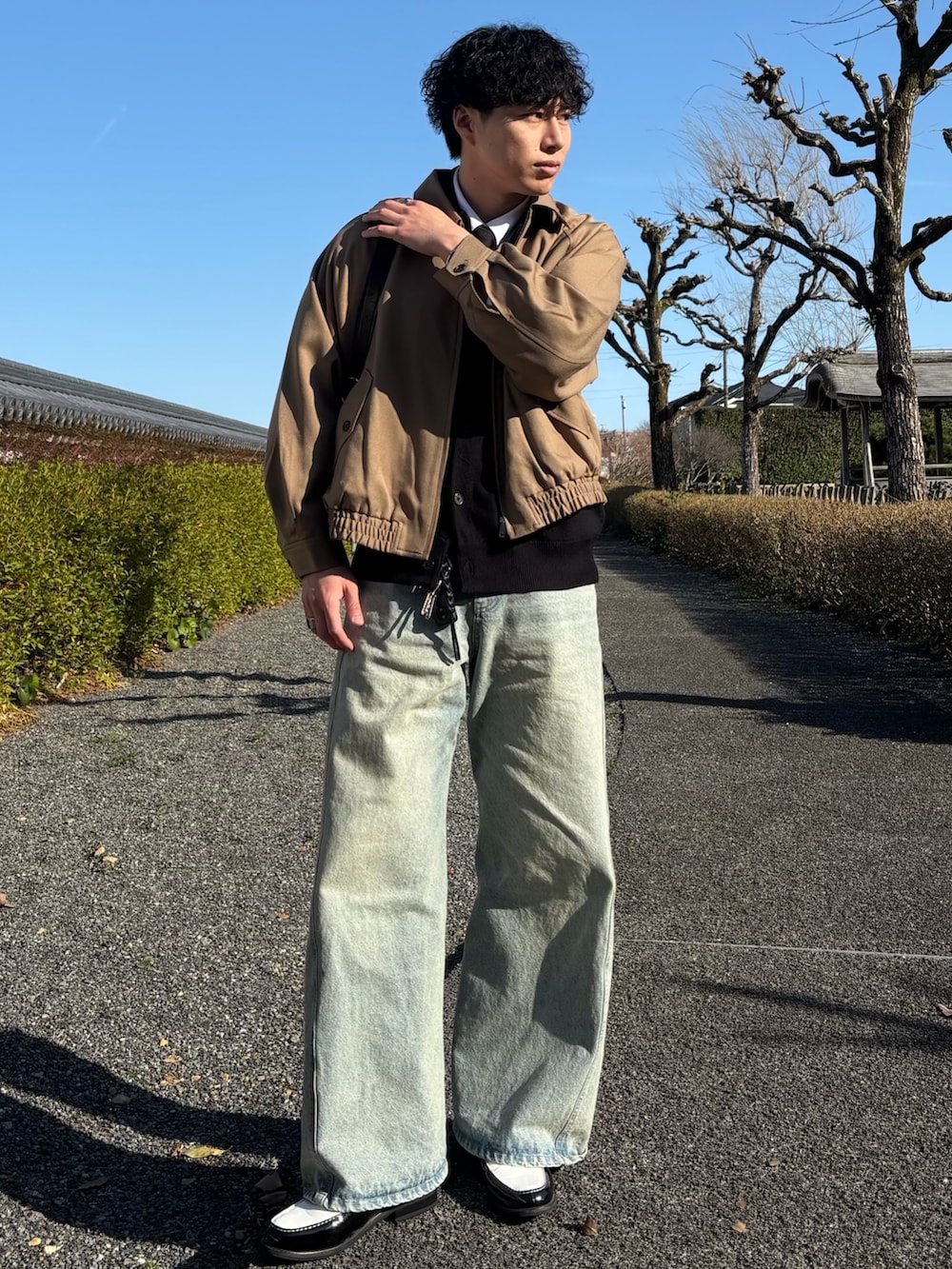 ブラック系のローファー、ブルー系のデニムパンツ、ブラック系のショルダーバッグを着用したメンズの春コーディネートの2枚目の写真