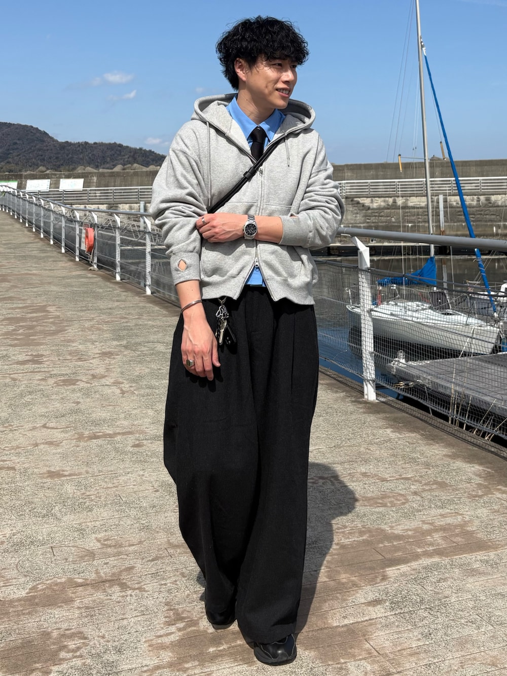 グレー系のスラックス、グレー系のパーカー、ブラック系のショルダーバッグを着用したメンズの春コーディネートの2枚目の写真