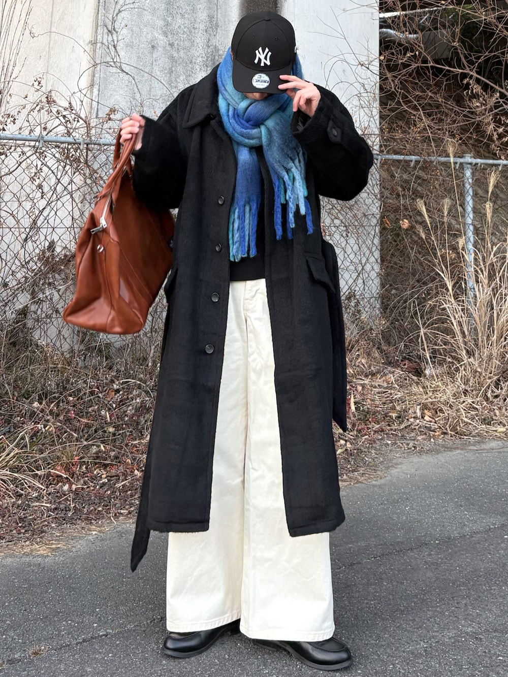 ブラック系のローファー、ブラック系のステンカラーコート、イエロー系のボストンバッグを着用したメンズの冬コーディネートの2枚目の写真