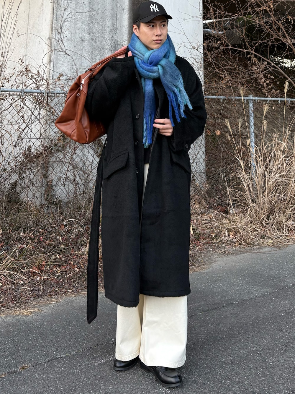 ブラック系のローファー、ブラック系のステンカラーコート、イエロー系のボストンバッグを着用したメンズの冬コーディネートの4枚目の写真