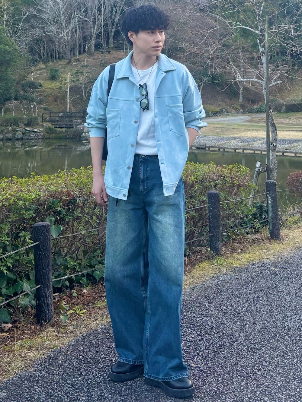 ブルー系のデニムパンツ、ブラック系のショルダーバッグ、ブラック系のドレスシューズを着用したメンズの春コーディネートの2枚目の写真